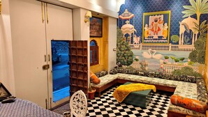 A room with a checkered floor, a wooden bench with cushions, a wall with a mural, and a wardrobe with a mirror. - Svarn By Experience Jaisalmer (Jaisalmer)