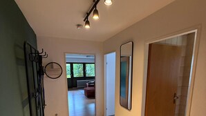 Un pasillo con piso de madera, alfombra gris, banca negra, espejo y puerta que da a otra habitación.
