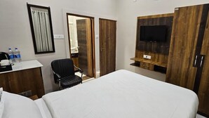 A hotel room with a bed, a desk with a chair, a TV mounted on a wooden panel, and a wardrobe. - Krishna Homestay (Varanasi)