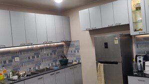 A kitchen with grey cabinets, a stainless steel refrigerator, a microwave, and a patterned backsplash. - Krishna Homestay (Varanasi)