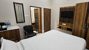 A hotel room with a bed, a desk with a chair, a TV mounted on a wooden panel, and a wardrobe. - Krishna Homestay (Varanasi)
