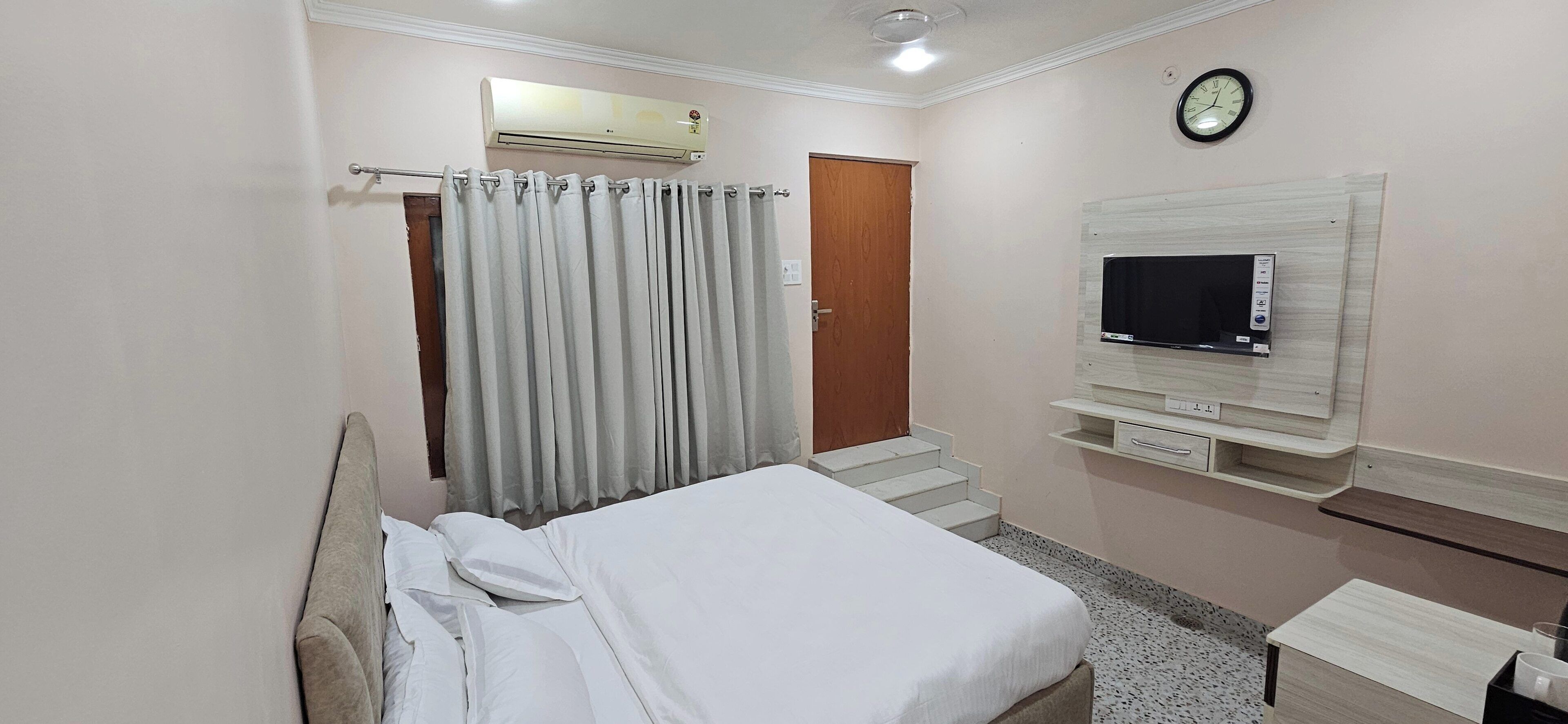 Una habitación de hotel con cama, televisor montado en la pared, cortina, puerta y escalera.