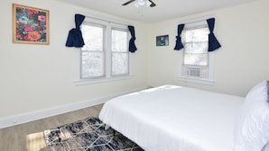 A bedroom with a bed, two windows with curtains, a ceiling fan, and a floor lamp.