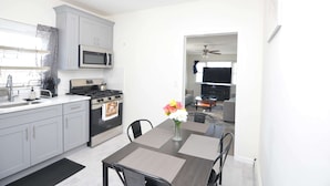 A modern kitchen with grey cabinets, a microwave, stove, and sink. There is a dining table with chairs and a vase of flowers.