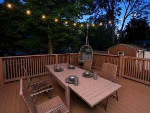 Une terrasse extérieure avec une table et des chaises, des guirlandes lumineuses et un fauteuil suspendu.