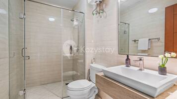 A modern bathroom with a glass shower enclosure, a white toilet, and a large sink with a mirror above.