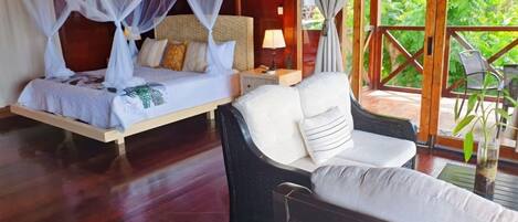 A bedroom with a bed, bedside table, and a view of lush greenery.