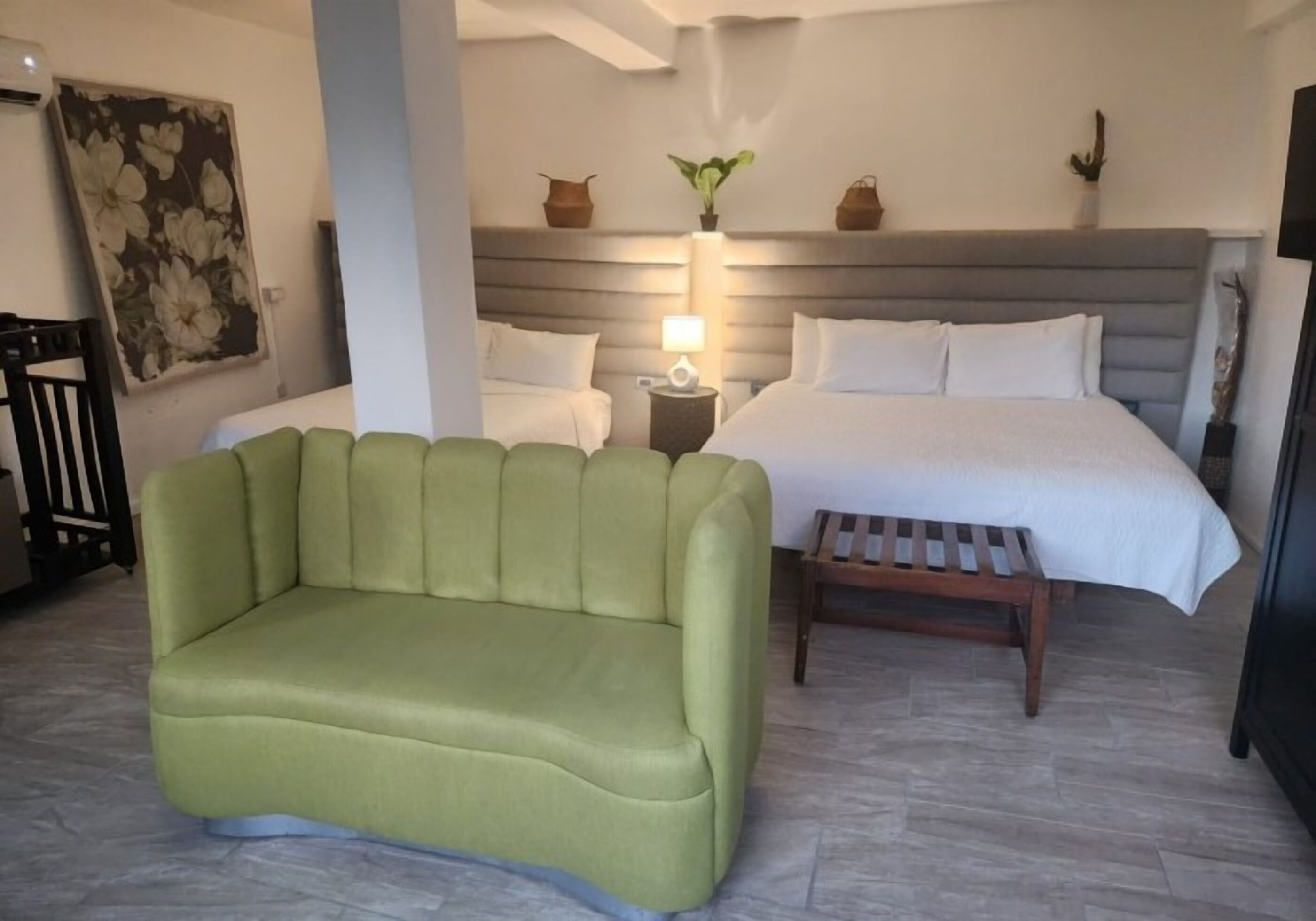Ein Hotelzimmer mit einem grünen Sofa, einem Bett mit weißen Leinentüchern, einem Nachttisch mit Lampe und einem großen Blumenbild an der Wand.