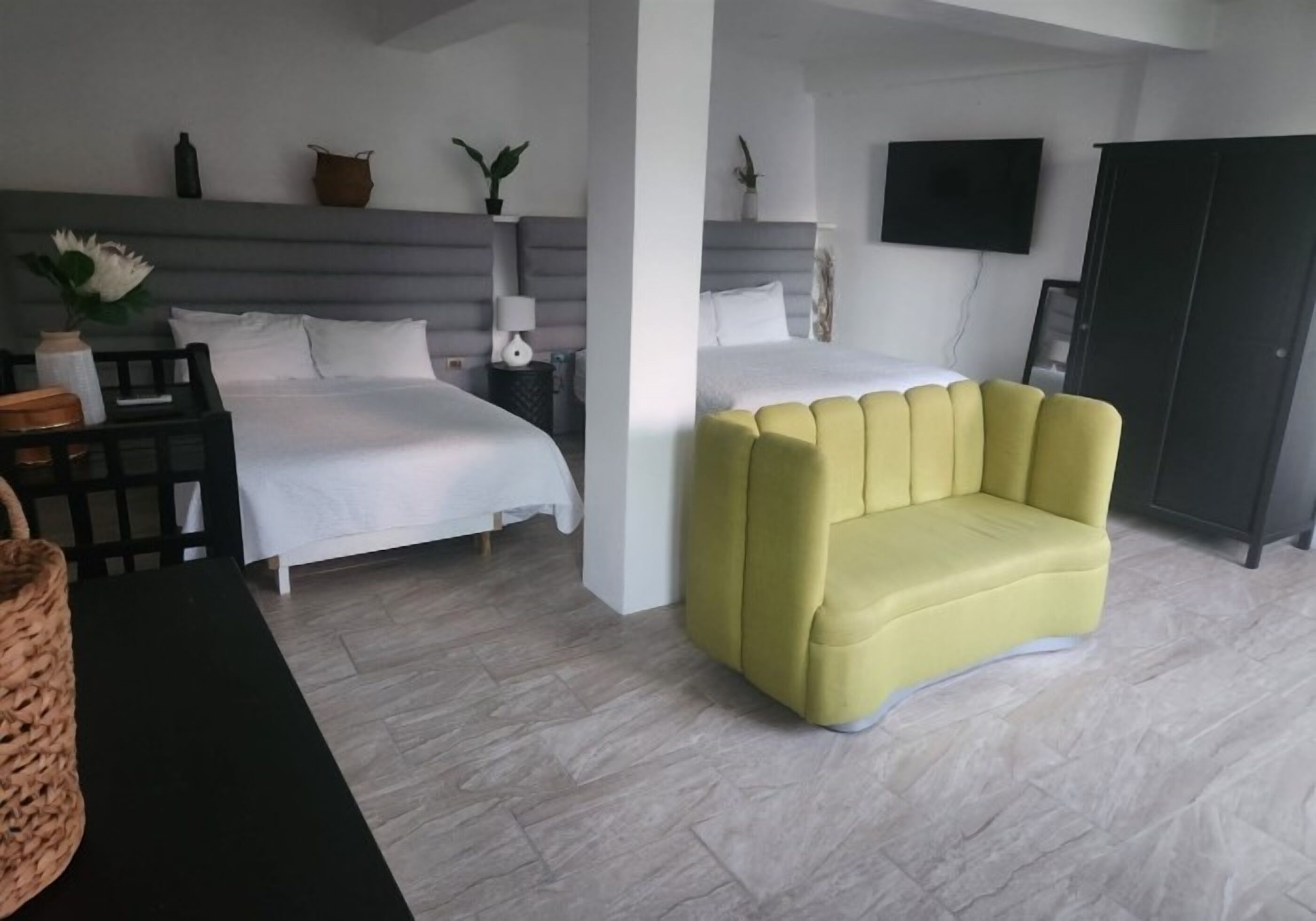 A modern hotel room with two beds, a yellow armchair, a TV, and a wardrobe.