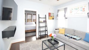 Un salon moderne comprenant un canapé, une table basse, un téléviseur fixé au mur, un ventilateur de plafond et une fenêtre avec des rideaux.