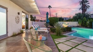 Un patio extérieur moderne avec une table en verre, des fauteuils de relaxation et une piscine.