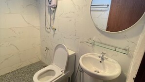 Een badkamer met toilet, bidet en wastafel, marmeren wanden en een spiegel.