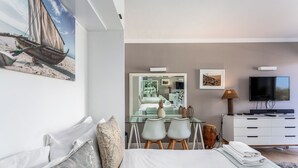 Une chambre à coucher moderne avec un grand lit, un bureau avec deux chaises, une télévision et un tableau représentant une scène de plage.