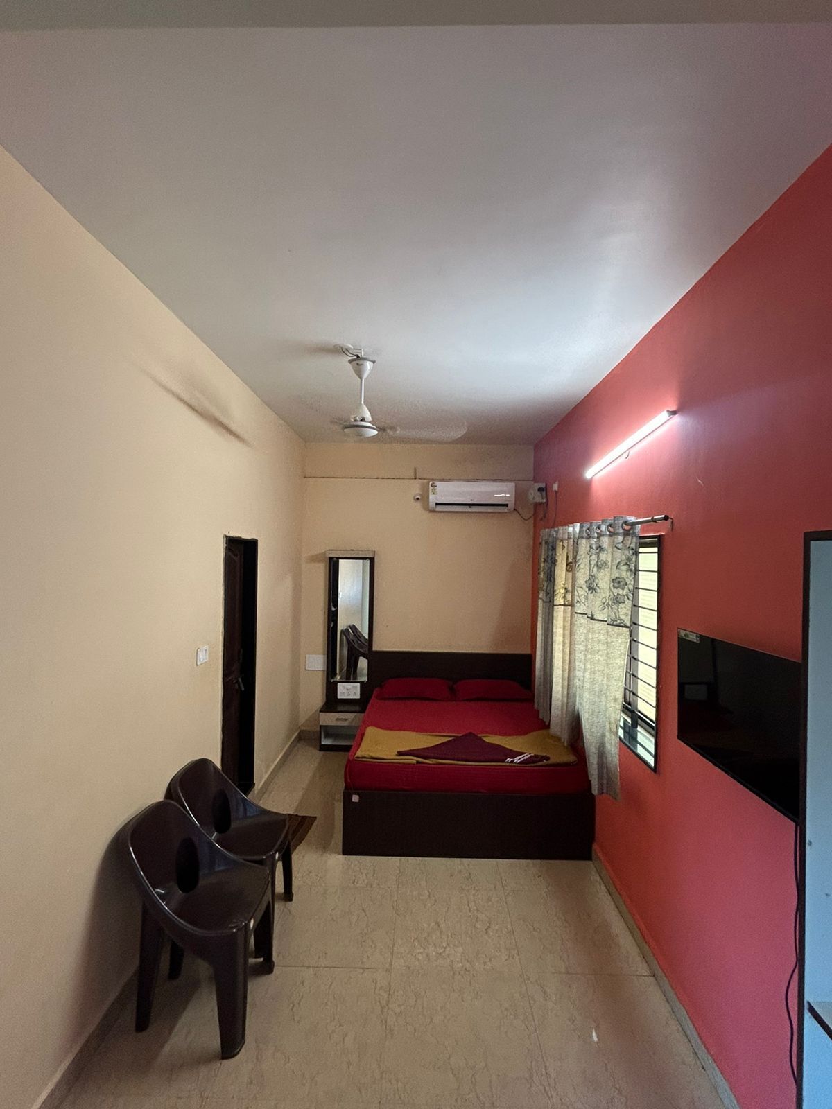A bedroom with a bed, a ceiling fan, an air conditioning unit, a TV, and a desk with a chair.