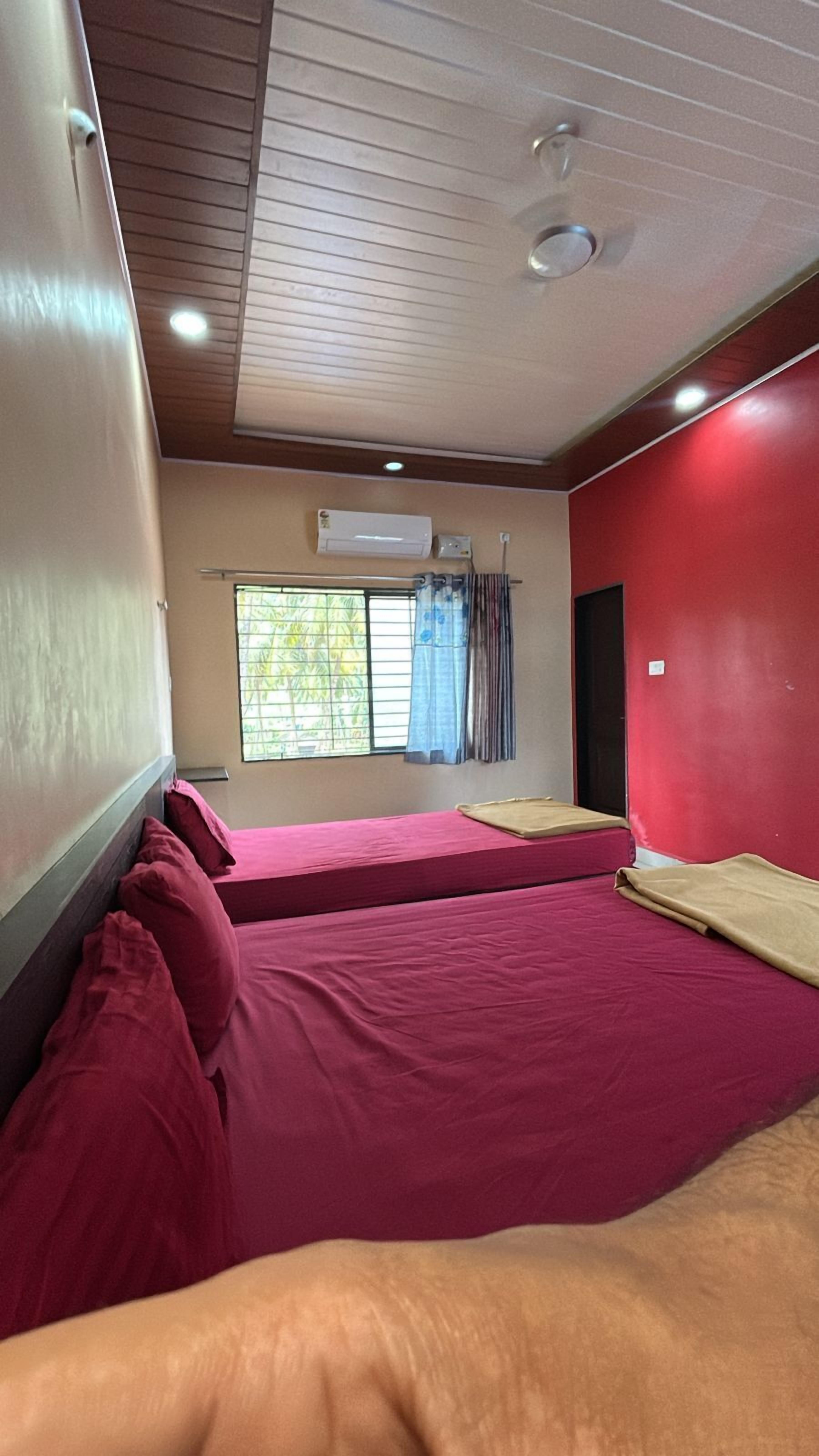 Een kamer met twee bedden, een raam met gordijnen, een airconditioning en een rode wand.