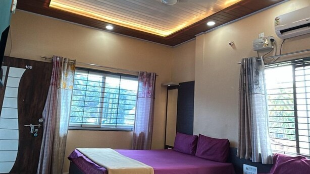 A hotel room with two beds, a ceiling fan, an air conditioning unit, and a window with curtains. - Seeta Residency (Gokarna)