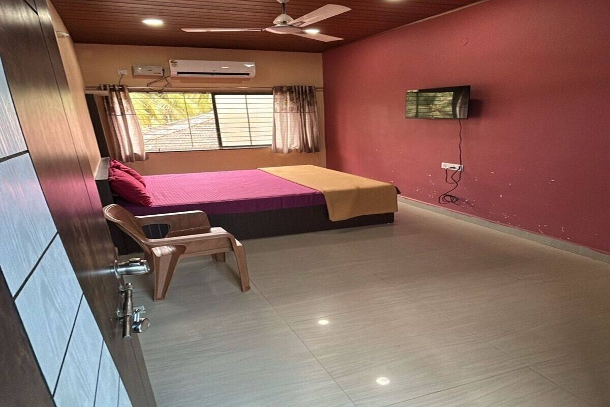 A bedroom with a bed, a chair, a ceiling fan, an air conditioning unit, and a television on the wall.