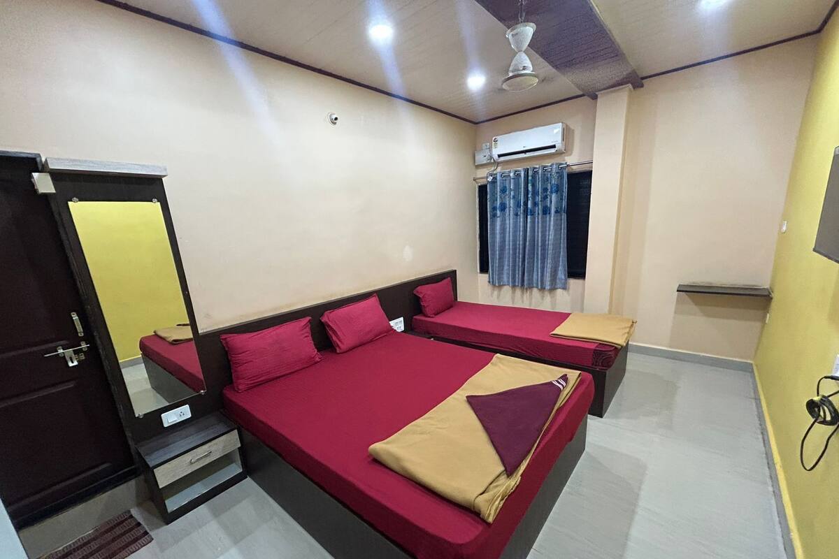 A room with two beds, a ceiling fan, an air conditioning unit, and a window with curtains.