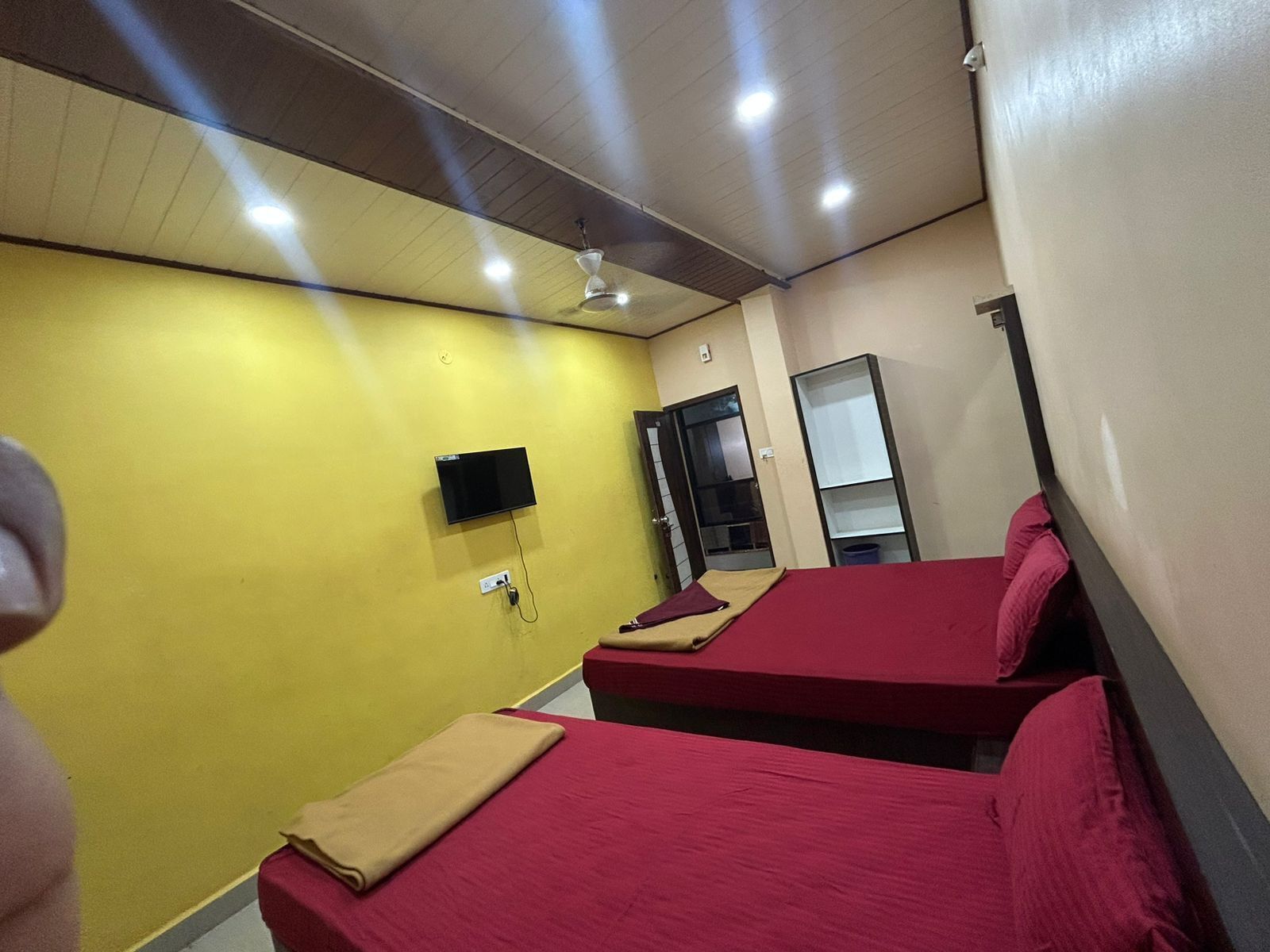 Una habitación con dos camas, ventilador de techo, televisor montado en la pared y una puerta que da a otra estancia.