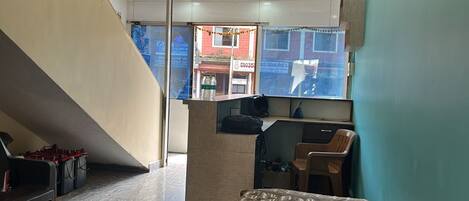 A room with a bed, a desk, and a chair. There is a window with a view of the outside.