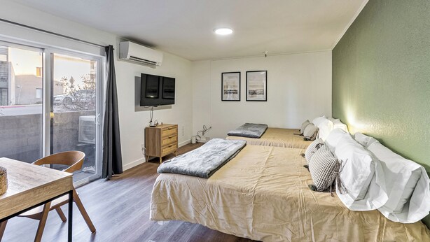 A modern hotel room with two beds, a wooden dresser, a TV, and a balcony with a view of the city. - Cozy stay for 2: 5 Min Drive to Base,  Full Kitchen, Shared Hot Tub & Pool, Restaurants Nearby! (Park City)