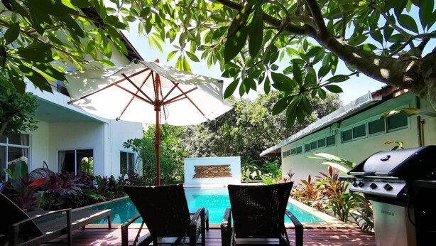 A deck with two chairs and a grill, overlooking a swimming pool and lush greenery. - Nakara Samui-Deluxe beach front (Amphoe Ko Samui)