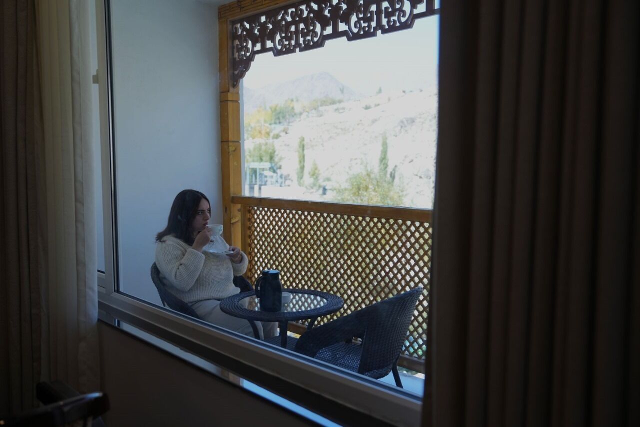 A person sitting at a table by a window with a view of a mountainous landscape.