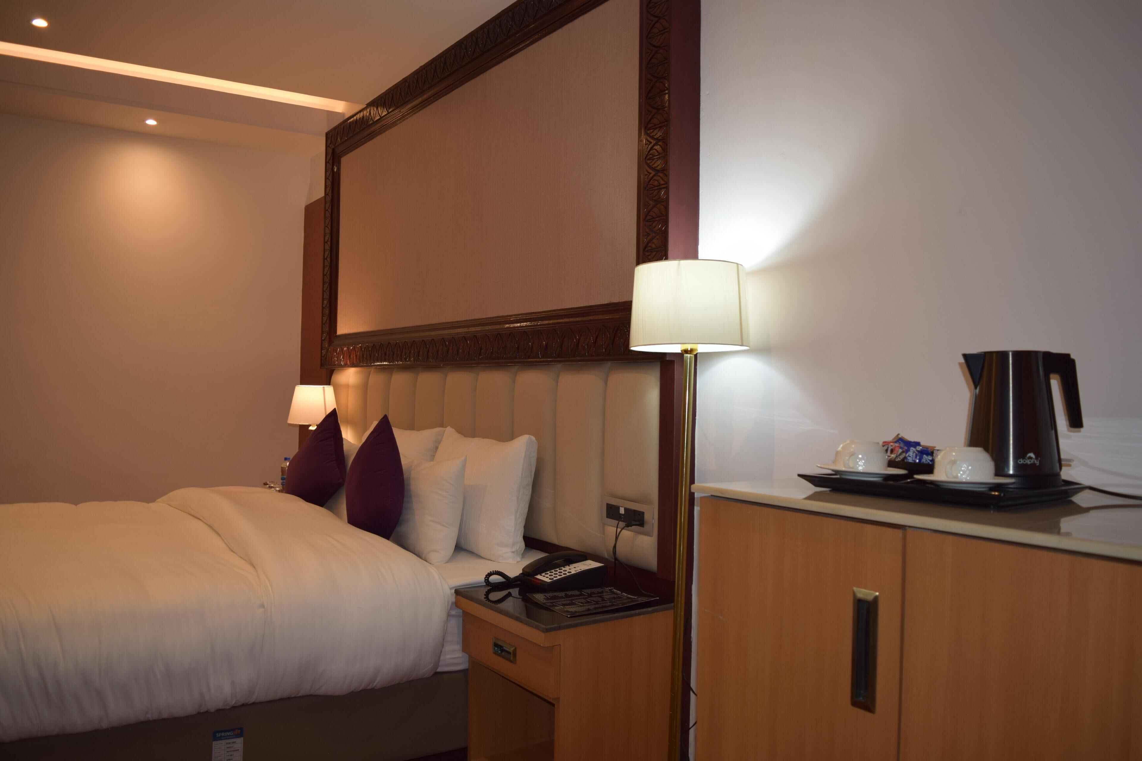 Una habitación de hotel con cama, mesita de noche, lámpara y cafetera.