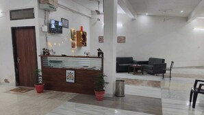 A reception area with a wooden counter, potted plants, a sofa, and a trash bin. - Hotel Raj Villas Palace (Jodhpur)