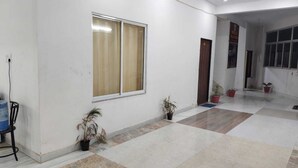 A spacious hallway with a tiled floor, a window with curtains, and potted plants. - Hotel Raj Villas Palace (Jodhpur)