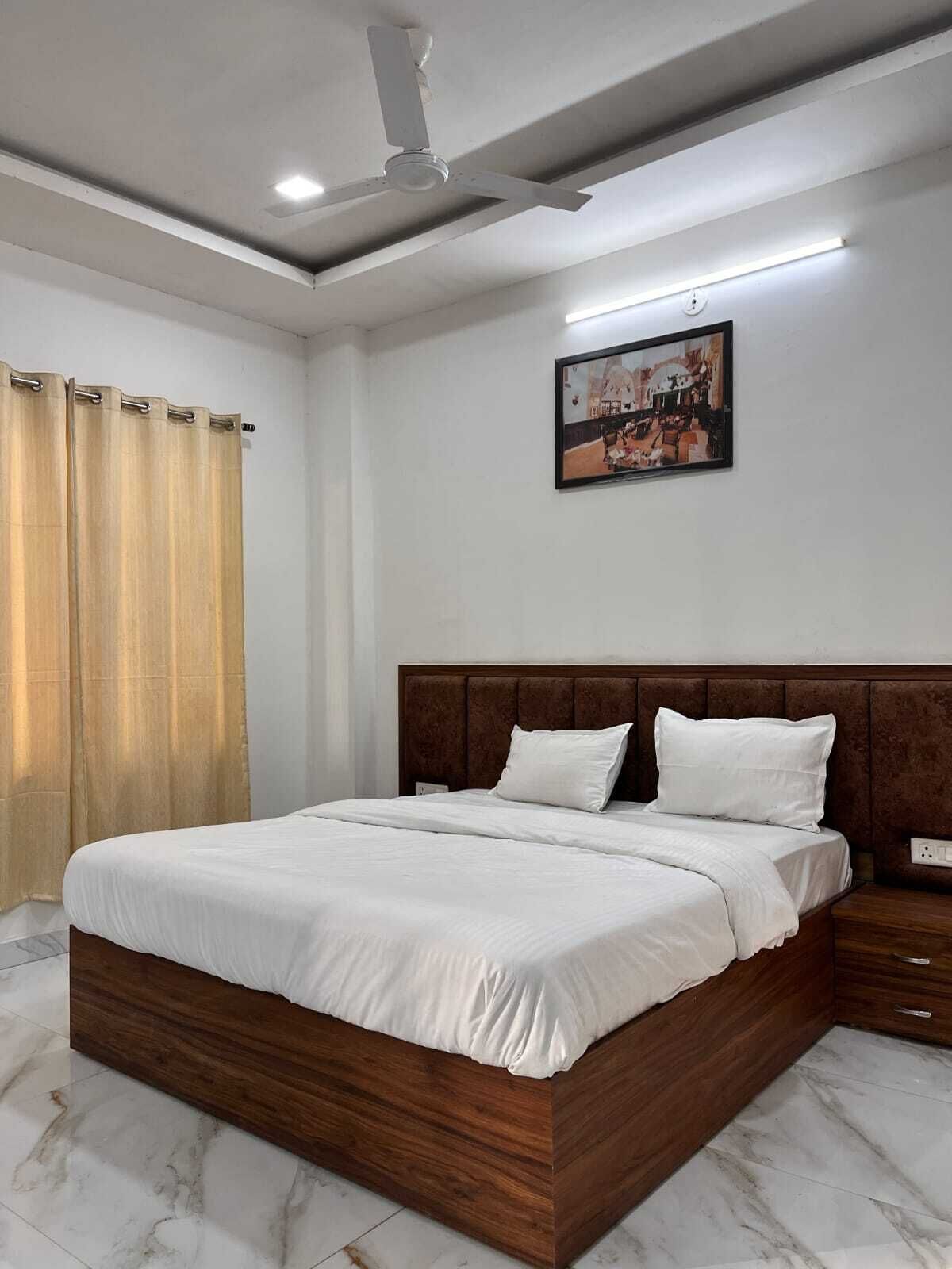 Um quarto com cama de madeira, roupa de cama branca, ventilador de teto, quadro na parede e janela com cortinas.