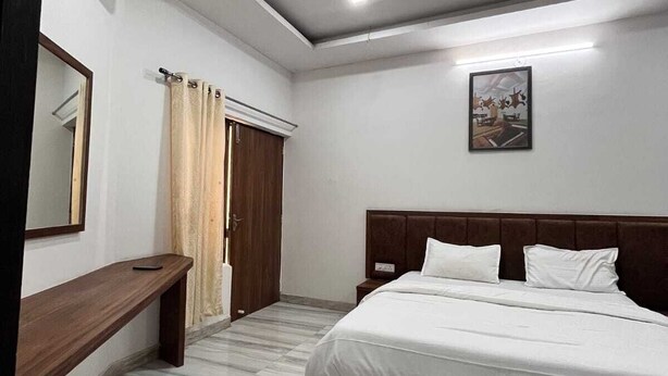 A bedroom with a large bed, a wooden headboard, a bedside table, a mirror, and a ceiling light. - Hotel Raj Villas Palace (Jodhpur)