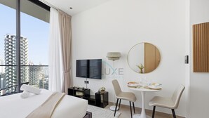 Een moderne hotelkamer met een groot bed, een televisie, een ronde spiegel, een eettafel met stoelen en uitzicht op de stad.