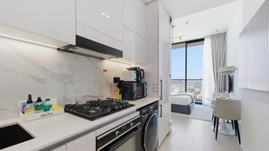Een moderne keuken met een gasfornuis, oven en magnetron. Er is een wasmachine en een eethoek met een tafel en stoelen.