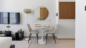 Een moderne woonkamer met een flatscreen televisie, een ronde spiegel, twee stoelen, een klein tafeltje met een decoratief object en een vloerlamp.