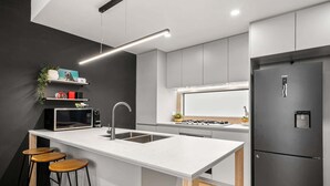 A modern kitchen with a central island, stainless steel appliances, and a black refrigerator. - Chic Home with BBQ & Outdoor Dining (Carnegie)