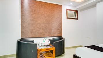 A room with a bed, a desk with a chair, a wall-mounted air conditioner, and a window with a brown blind.