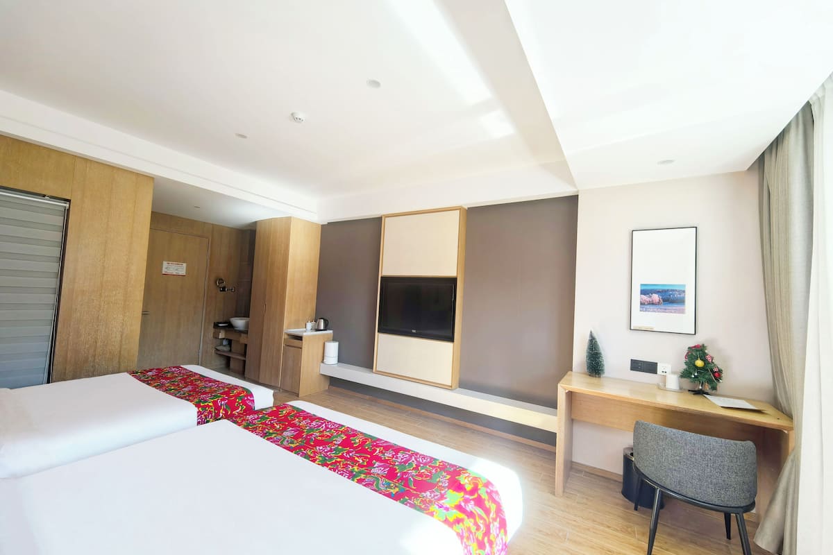 Habitación de hotel con cama, escritorio, silla, una planta pequeña y un cuadro en la pared.