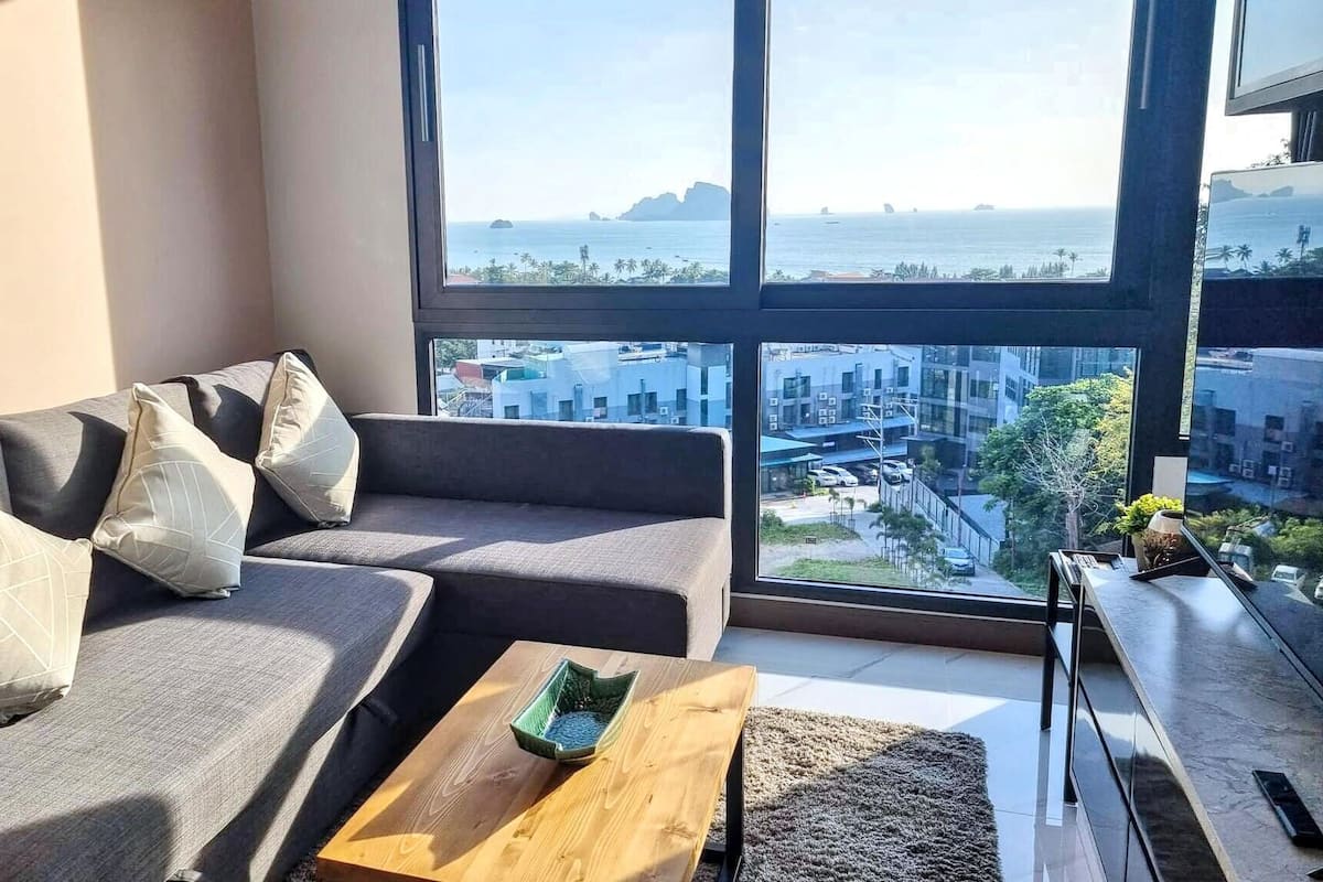 A modern living room with a large window, a grey sofa, and a wooden coffee table.