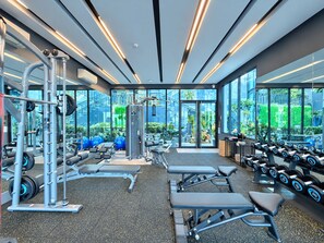 A modern gym with various exercise equipment, large windows, and a view of greenery outside. - Silk Ao Nang Condominium (Krabi)