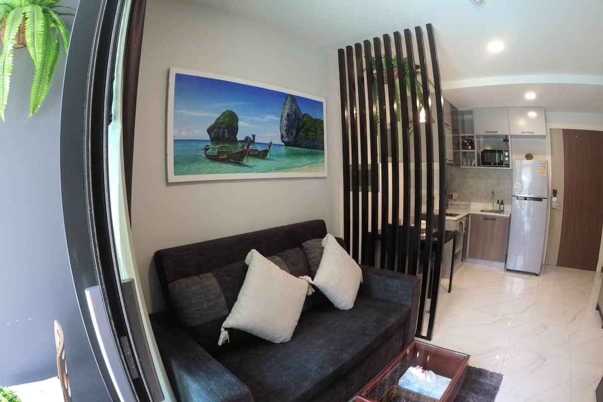 A modern living room with a dark sofa, a glass coffee table, and a kitchen area with a refrigerator and microwave.