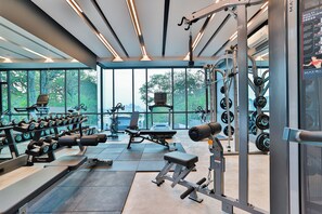 A modern gym with various exercise equipment, large windows, and a view of greenery. - Silk Ao Nang Condominium (Krabi)