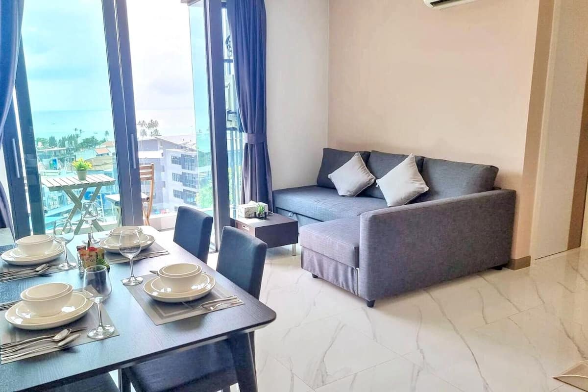 A dining area with a table set for four, a grey sofa, and a view of the ocean.