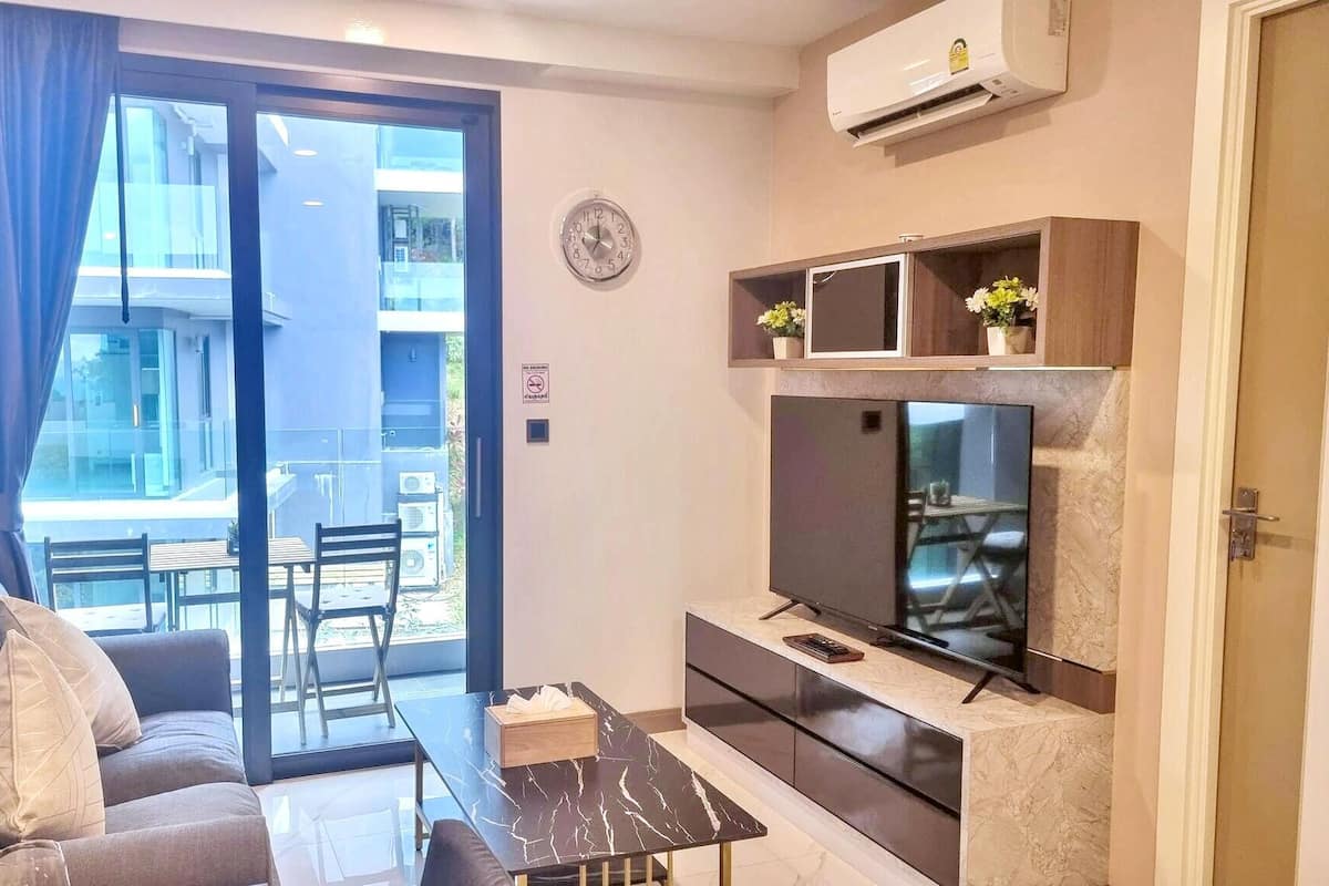 A living room with a sofa, a TV, a coffee table, and a balcony with a view.