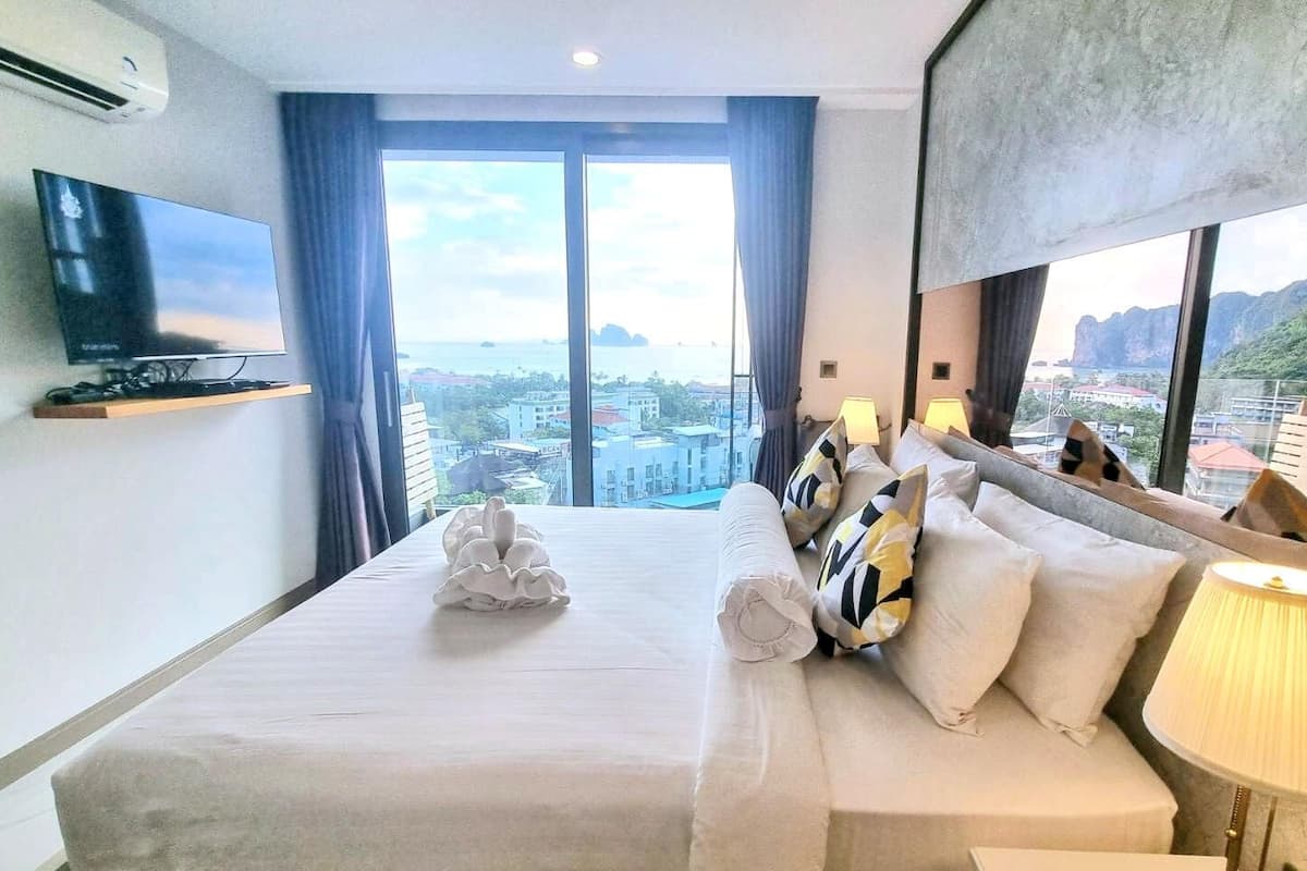 A hotel room with a large bed, a TV on the wall, and a view of the city through the windows.