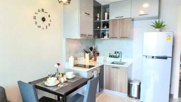 A modern kitchen with a dining area, a clock on the wall, and a refrigerator.