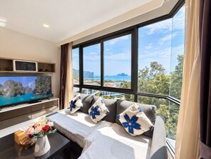Una habitación moderna con un ventanal grande, un televisor de pantalla plana, un sofá con almohadones decorativos y una mesita con un florero.