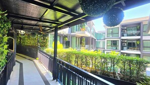 A covered walkway with a metal railing, surrounded by lush greenery and modern buildings with large windows and balconies. - Silk Ao Nang Condominium (Krabi)