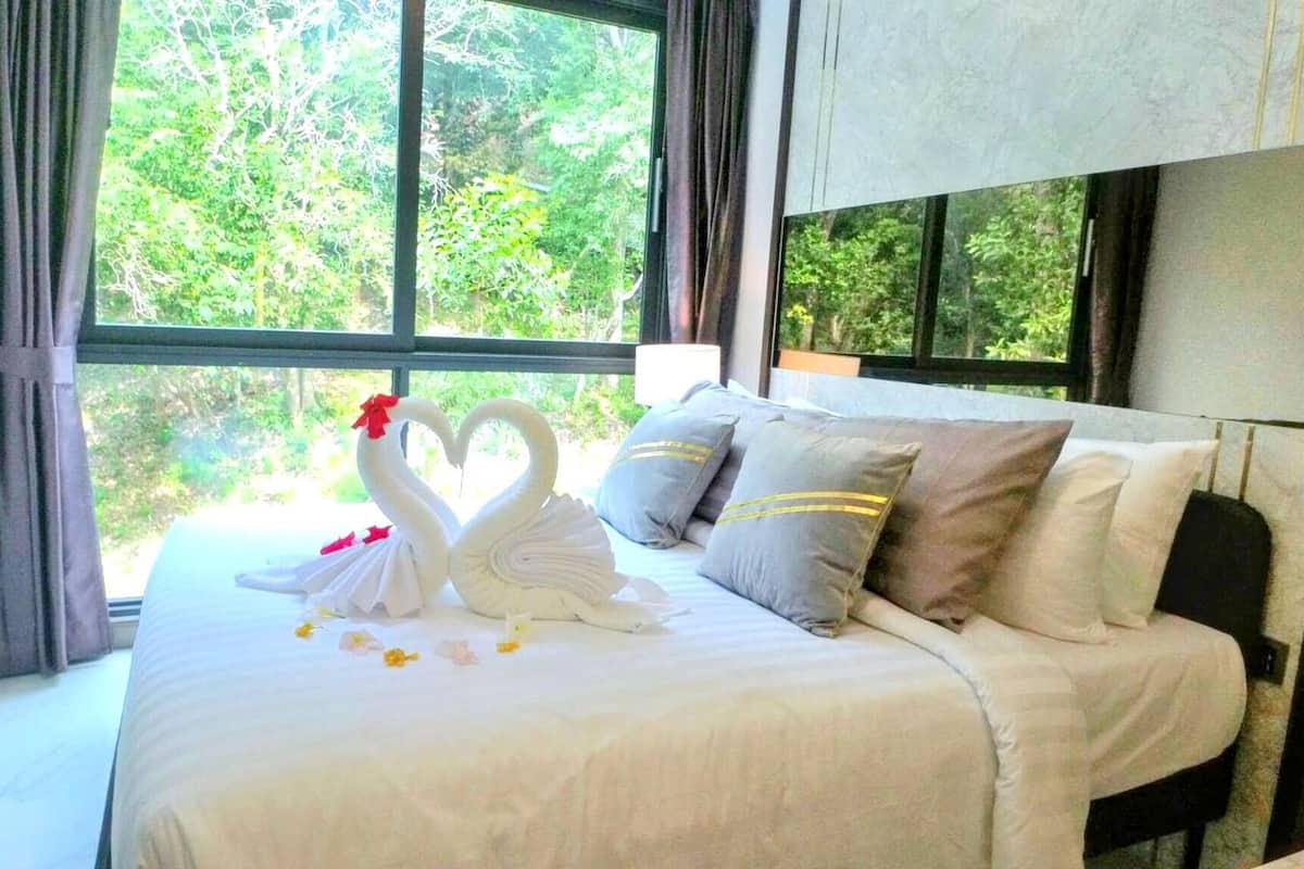A bed with a white bedspread, two swan-shaped pillows, and a heart-shaped decoration made of flowers.