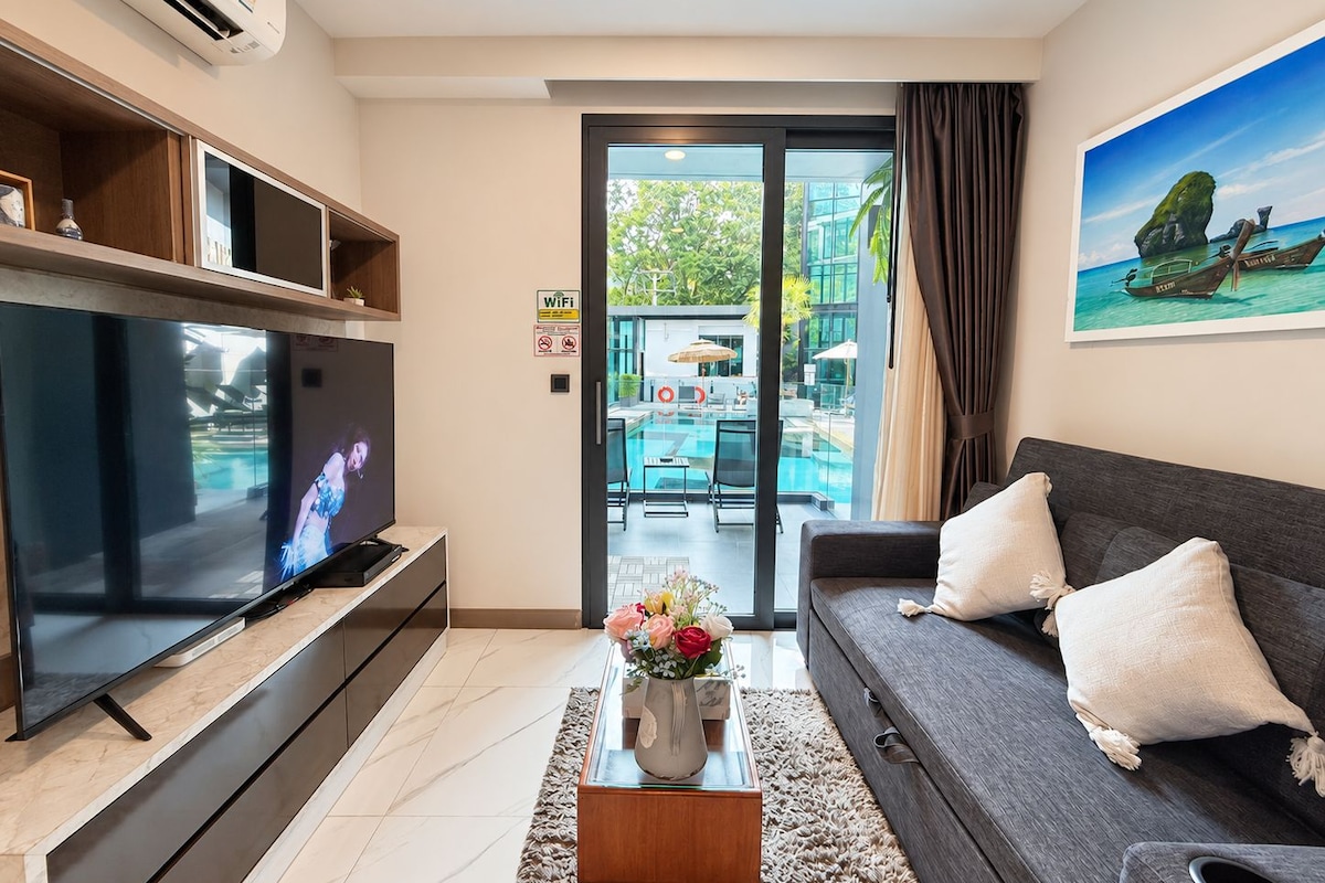 Una sala moderna con una televisión de pantalla plana, un sofá, una mesita de centro con flores y vistas a una zona de piscina exterior.
